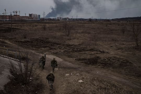 Soldaten gehen einen Weg entlang, während Rauch in Irpin nordwestlich von Kiew aufsteigt.