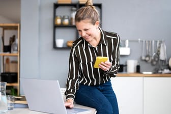 Eine Frau arbeitet in ihrer Küche am Laptop (Symbolbild): Am 20. März enden die bislang bestehenden Corona-Schutzmaßnahmen zum Großteil.