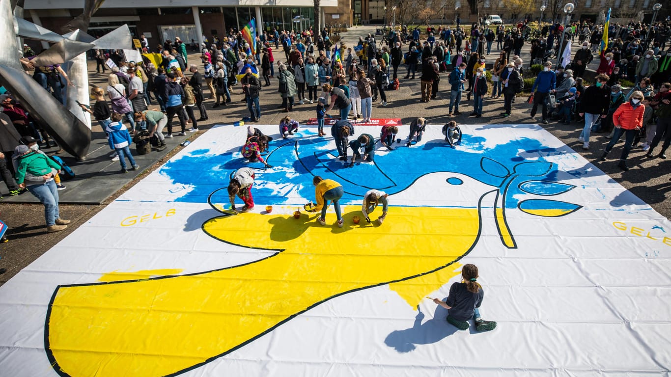Stuttgart: Kinder bemalen bei der Demonstration gegen den Krieg eine Friedenstaube in den Farben der Ukraine.