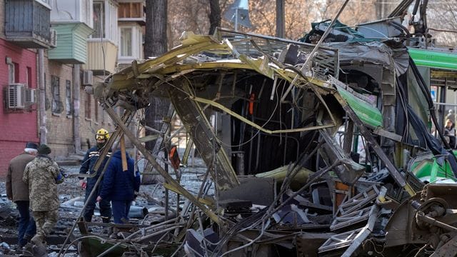 Soldaten stehen nach einem Bombenangriff auf einer Straße in Kiew neben einer zerstörten Straßenbahn.