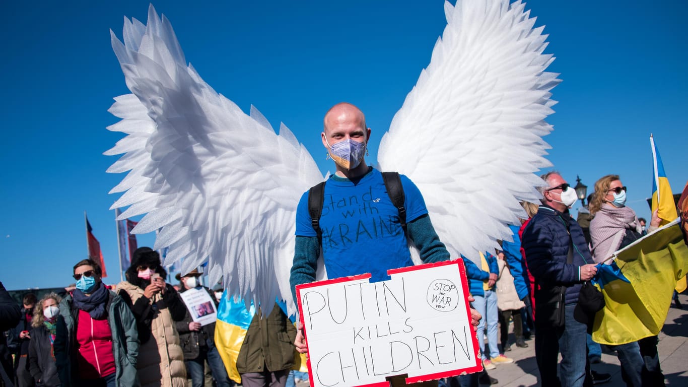 Ein Teilnehmer der Demonstration gegen den Ukraine-Konflikt steht auf dem Jungfernstieg, trägt nachgebaute Flügel einer Friedenstaube.
