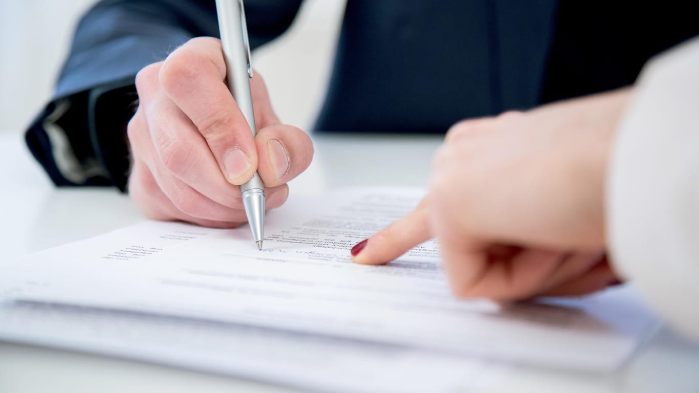 Ein Mann unterschreibt einen Vertrag (Symbolbild): In manchen Arbeitsverträgen finden sich Klauseln zur Mehrarbeit.