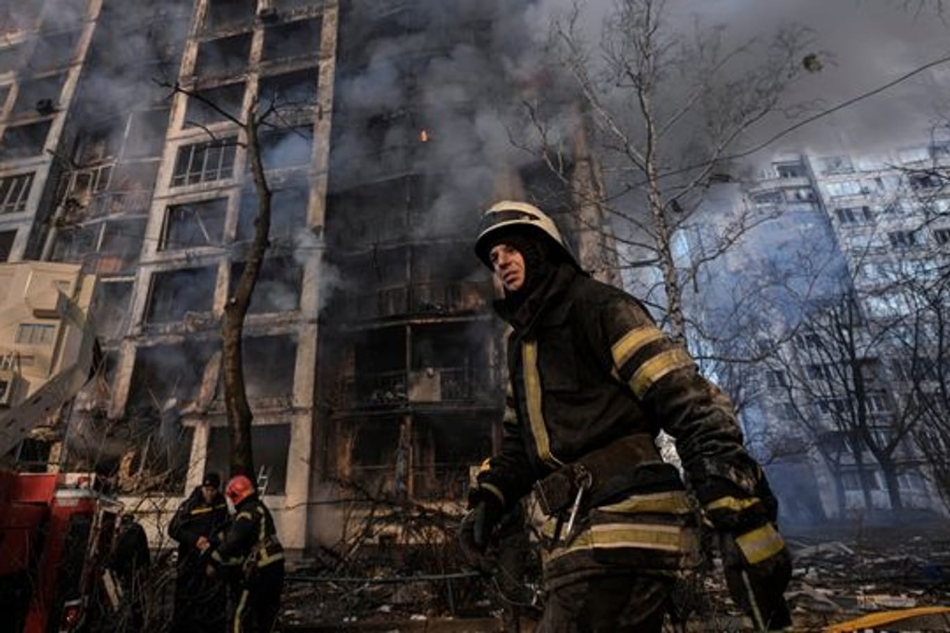 Einsatzkräfte der Feuerwehr stehen in Kiew vor einem brennenden Wohngebäude, dass durch Bombenbeschuss des russischen Militärs zerstört wurde.