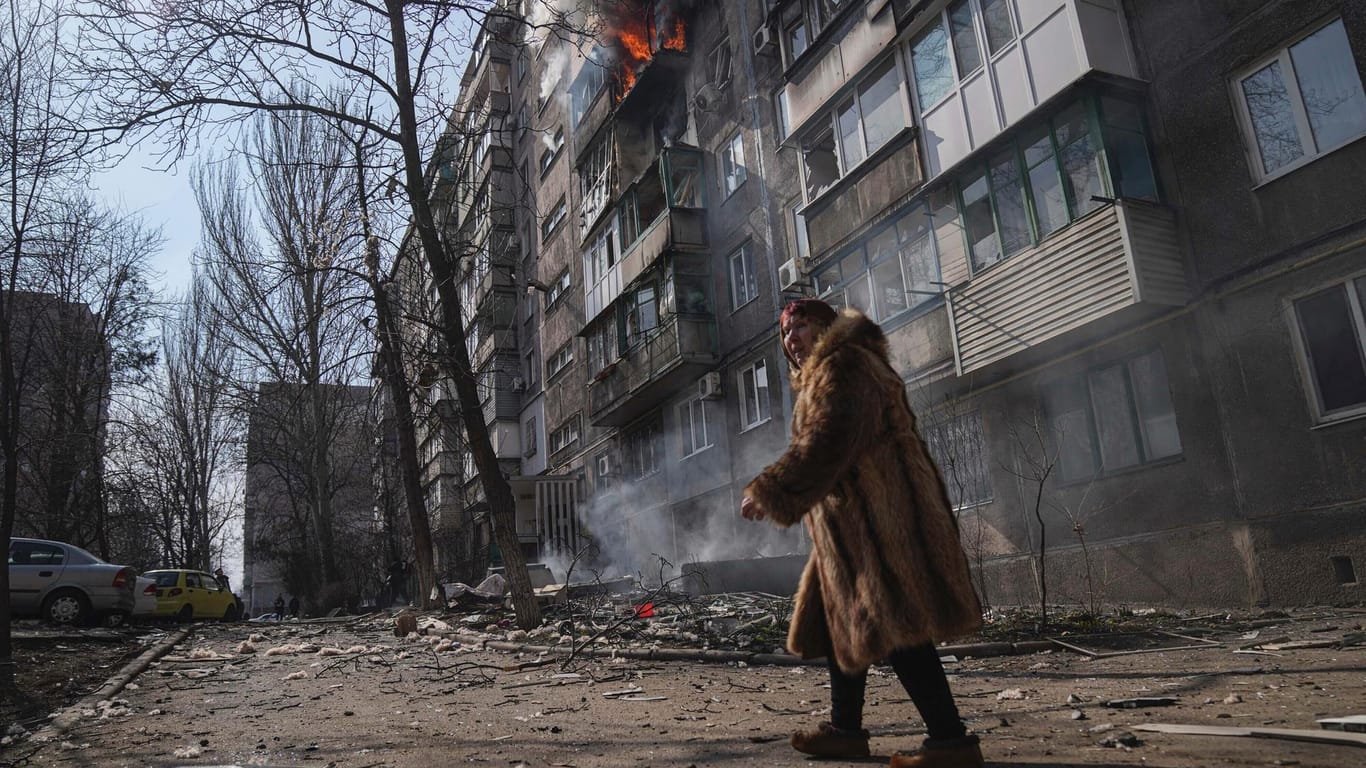 Eine Frau geht an einem brennenden Wohnhaus vorbei, nachdem es in Mariupol beschossen wurde.