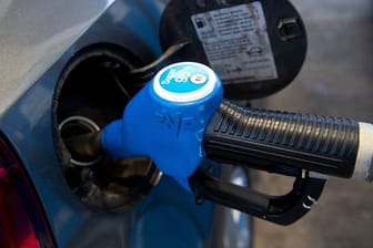 Eine Zapfpistole mit der Aufschrift "Super 95" steckt an einer Tankstelle in der Tanköffnung eines Fahrzeugs.