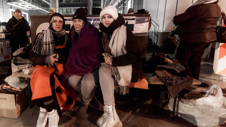 Drei Frauen harren über Nacht vor Ort aus, um ihren Platz auf einer selbst organisierten Warteliste, und damit die Chance auf die Bearbeitung ihrer Anträge in der Behörde am nächsten Tag, nicht zu verlieren.