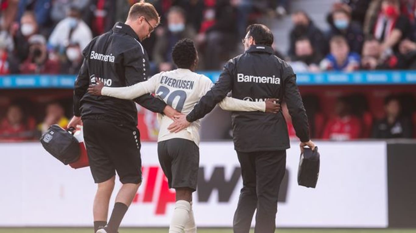 Leverkusens Jeremie Frimpong (M) wird von Betreuern gestützt, während er verletzt den Platz verlässt.