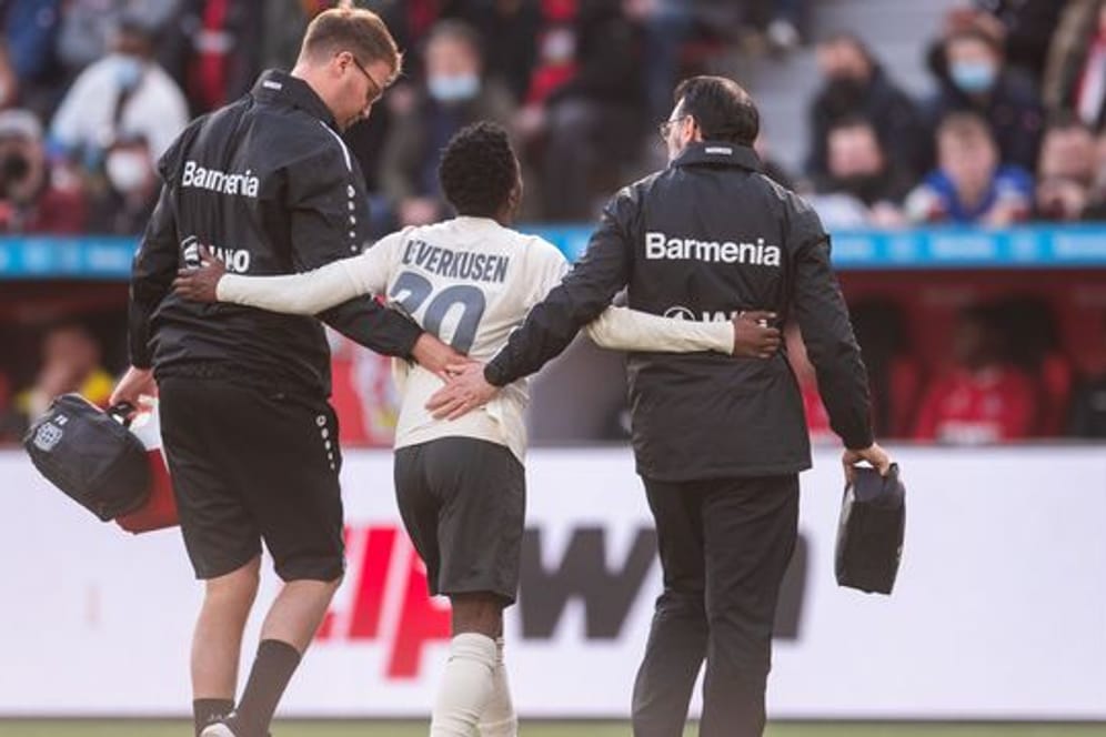 Leverkusens Jeremie Frimpong (M) wird von Betreuern gestützt, während er verletzt den Platz verlässt.