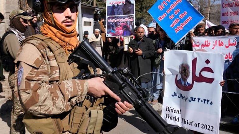 Ein bewaffneter Taliban Kämpfer steht während einer Demonstration neben afghanischen Demonstranten.