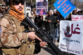 Ein bewaffneter Taliban Kämpfer steht während einer Demonstration neben afghanischen Demonstranten.