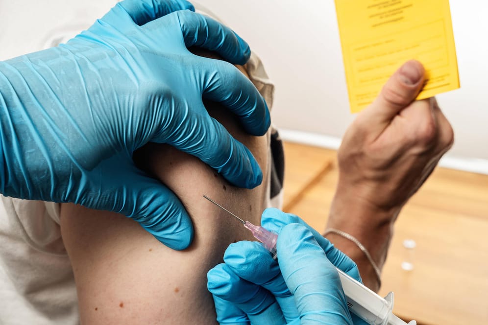 Arzt impft Person, die Impfpass in der Hand hält (Symbolbild): Bis zum 15. Juni gilt eine Übergangsfrist.