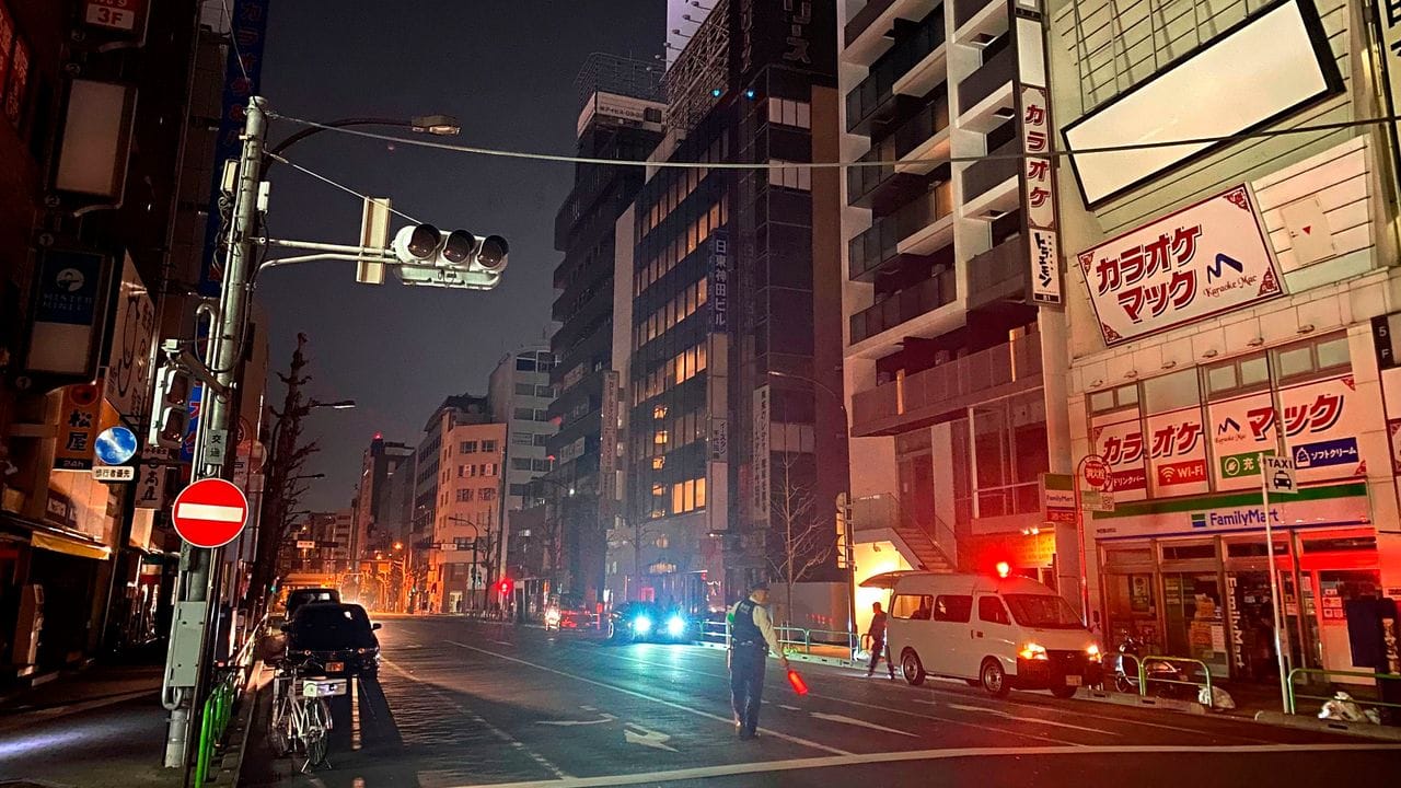 Ein Polizist steht während eines Stromausfalls in Tokio auf der Straße und leitet den Verkehr. Ein Polizist steht während eines Stromausfalls in Tokio auf der Straße und leitet den Verkehr.