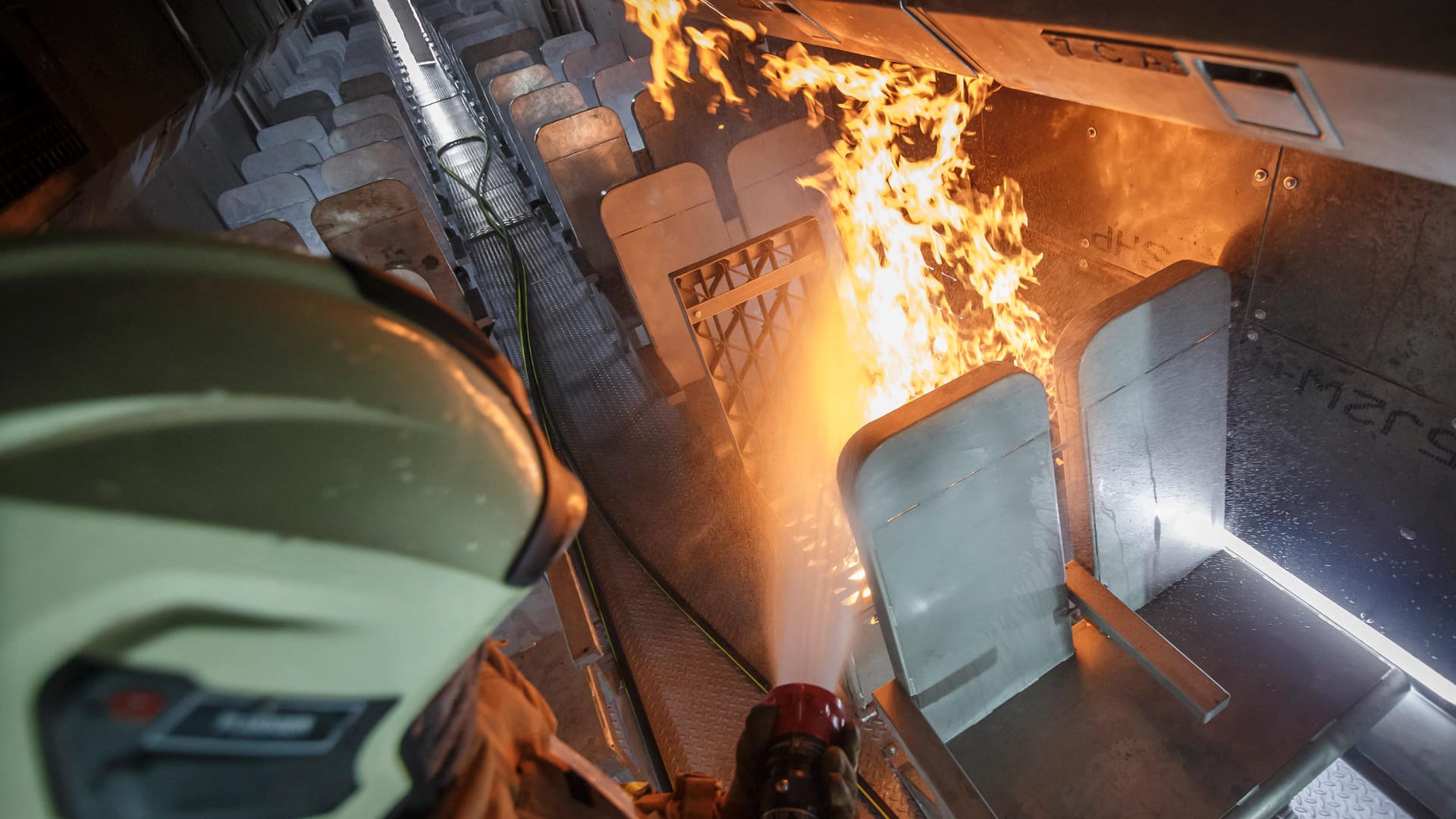 Ein Feuerwehrmann löscht eine Brandstelle, die einen Sitzplatz im Flugzeuginneren darstellen soll.