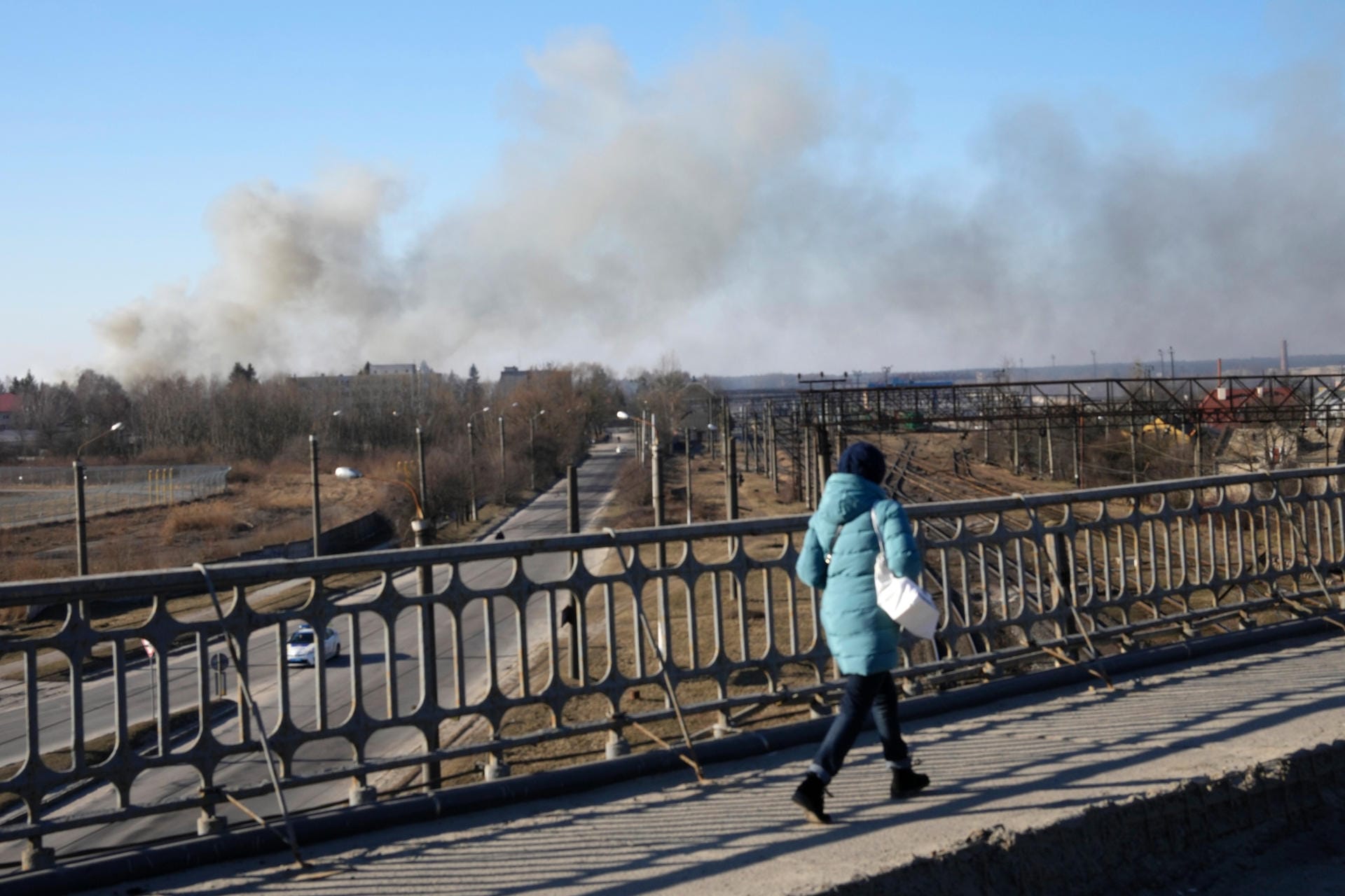 18. März 2022: Eine Frau geht über eine Brücke, während eine Rauchwolke nach einer Explosion aufsteigt. Nach Angaben des Bürgermeisters von Lwiw schlugen russische Raketen in der Nähe des Flughafens der Stadt ein.