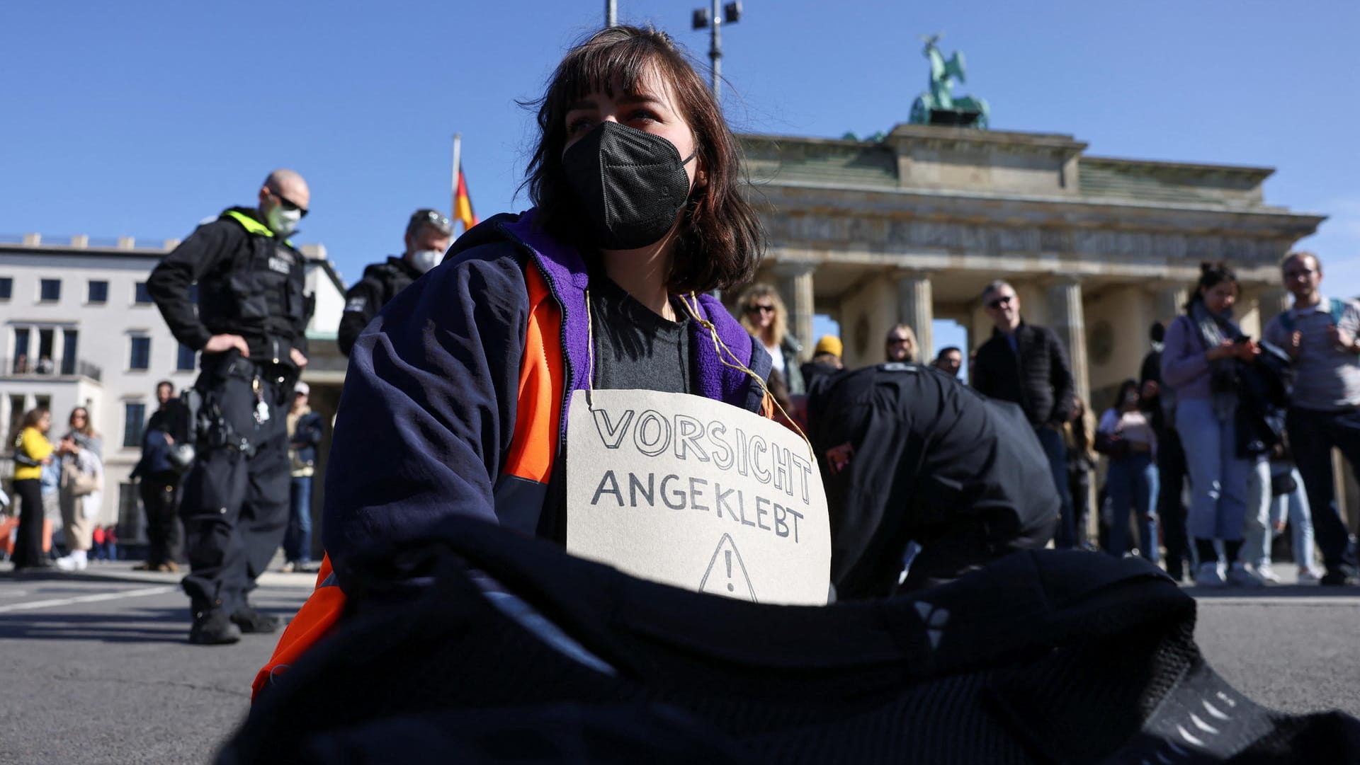 Eine Aktivistin der "Letzten Generation" vor dem Brandenburger Tor mit einem Schild um den Hals, das darauf hinweist, dass sie sich festgeklebt hat: Als Grund für die Proteste am Freitag gilt die erreichte 100-Tage-Marke der Bundesregierung. Eine Aktivistin der "Letzten Generation" vor dem Brandenburger Tor mit einem Schild um den Hals, das darauf hinweist, dass sie sich festgeklebt hat: Als Grund für die Proteste am Freitag gilt die erreichte 100-Tage-Marke der Bundesregierung.