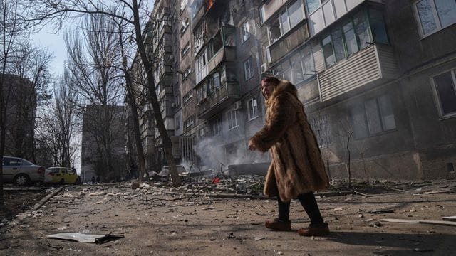 Eine Frau in Mariupol geht an einem brennenden Wohnhaus vorbei.