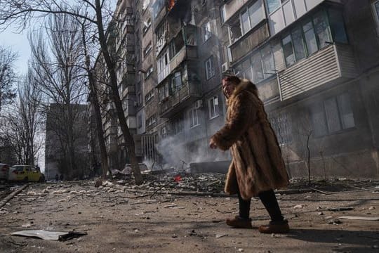 Eine Frau in Mariupol geht an einem brennenden Wohnhaus vorbei.