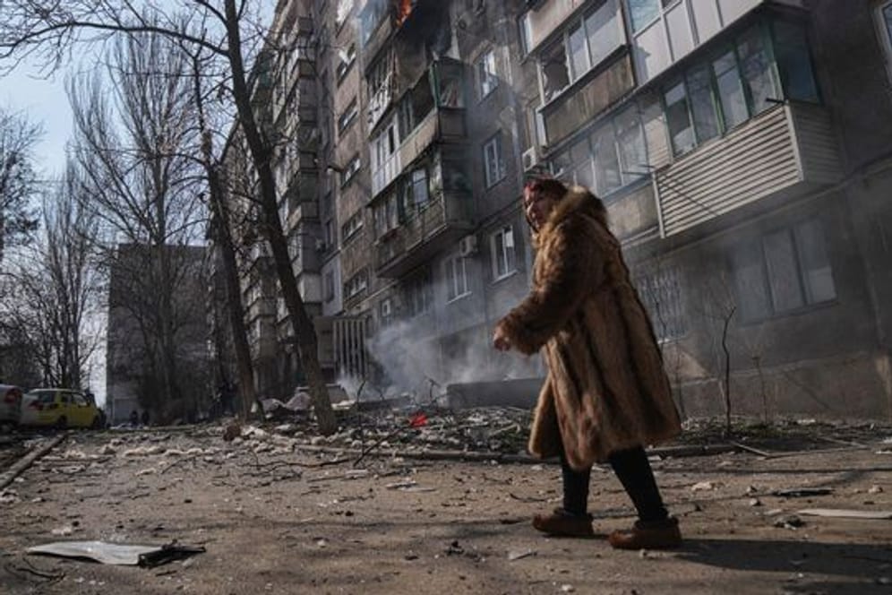 Eine Frau in Mariupol geht an einem brennenden Wohnhaus vorbei.