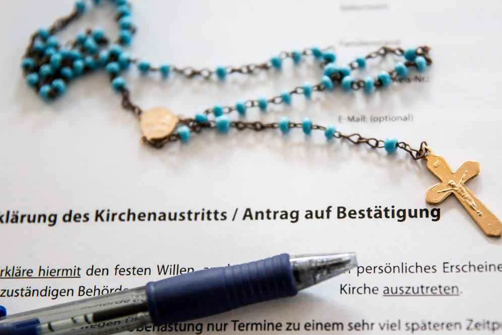 Ein Formular zur "Erklärung des Kirchenaustritts" und eine Kette mit einem Kreuz (Symbolbild): In Bayern nimmt die Zahl der Kirchenaustritte weiter zu.