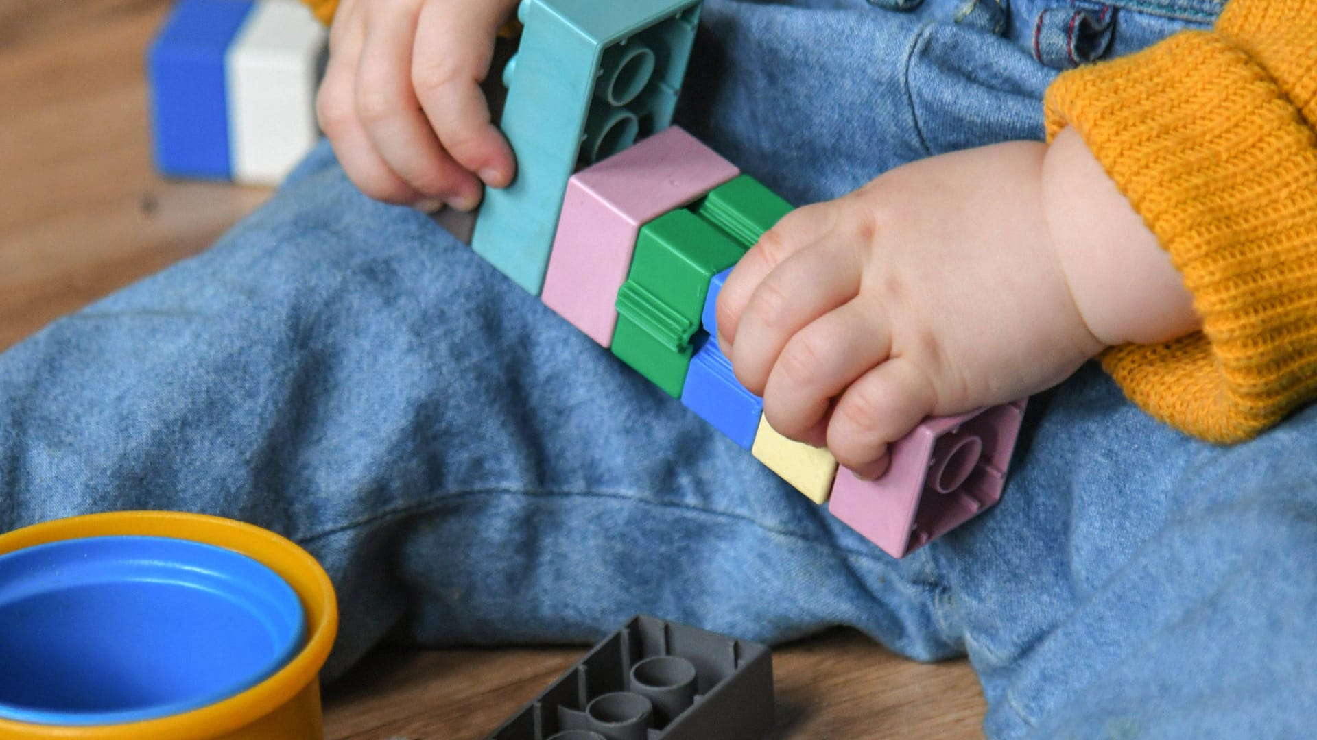 Ins Spiel vertieft sitzt ein Zweijähriger auf dem Boden und steckt Bausteine zusammen (Symbolbild): Für Kita-Kinder und ihre Eltern gibt es deutliche Corona-Lockerungen.