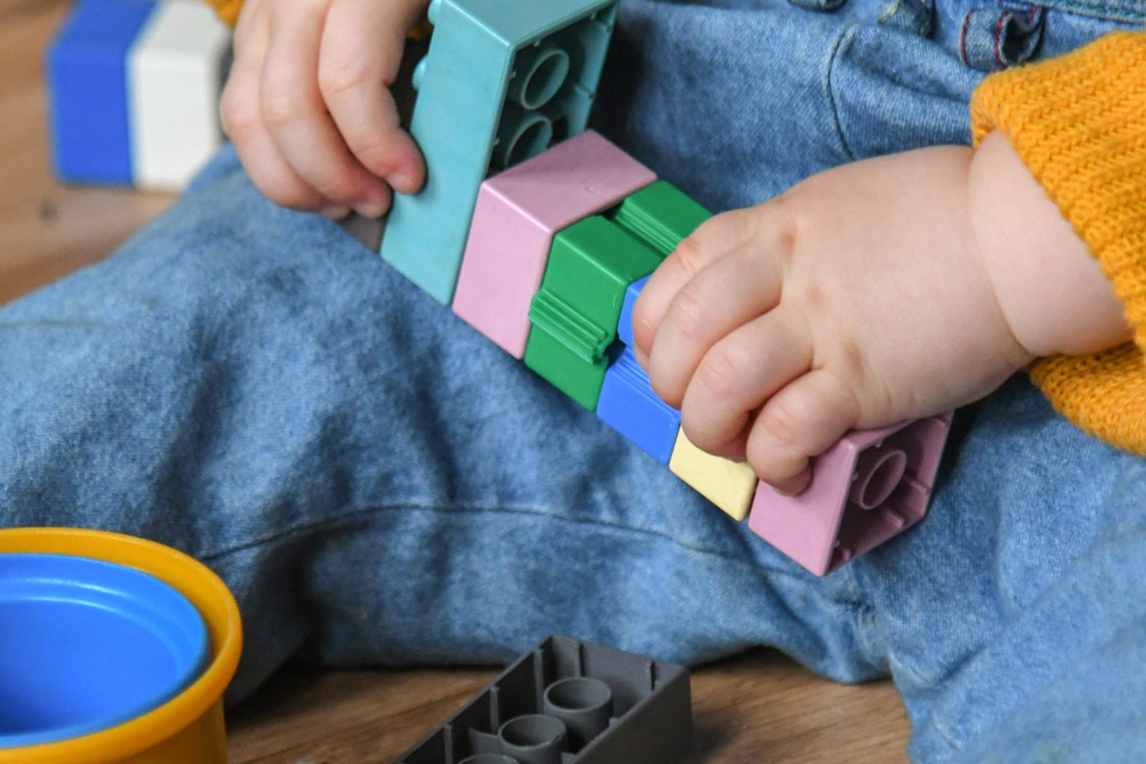 Ins Spiel vertieft sitzt ein Zweijähriger auf dem Boden und steckt Bausteine zusammen (Symbolbild): Für Kita-Kinder und ihre Eltern gibt es deutliche Corona-Lockerungen.