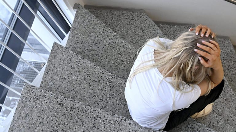 Eine verzweifelte Frau sitzt auf der Treppe im Hausflur (Symbolbild): Die durchschnittlichen Krankschreibungstage wegen psychischer Krankheiten nehmen in Hessen zu.