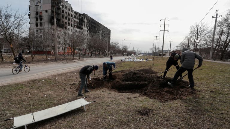 Einwohner der zerschossenen Stadt Mariupol heben ein Grab aus.