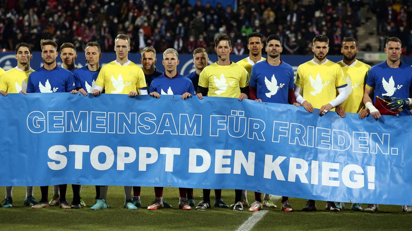 Die Teams vom HSV und dem 1. FC Nürnberg tragen die Friedensshirts und halten ein Banner hoch (Archivbild): Die Shirts können nun ersteigert werden.