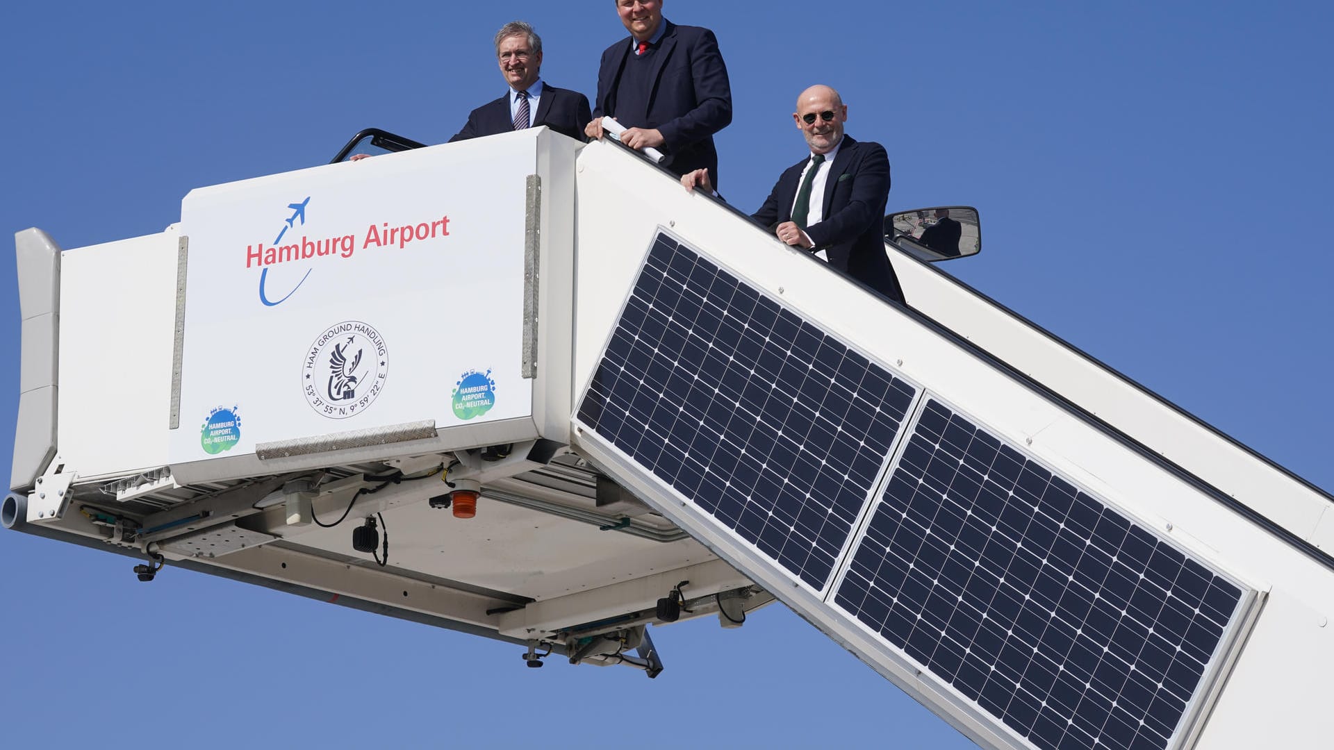 Michael Eggenschwiler (l-r), Vorsitzender der Geschäftsführung am Hamburg Airport, Andreas Dressel, und Michael Westhagemann stehen auf einer Passagiertreppe, an der Solarpanel angebracht sind: Der Hamburger Flughafen hat sich als erster deutscher Airport für CO2-neutral erklärt.