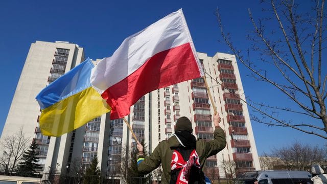 Ein Mann schwenkt während einer Demonstration in Warschau die ukrainische und die polnische Flagge vor einem Gebäude, in dem russische Diplomaten untergebracht sind.