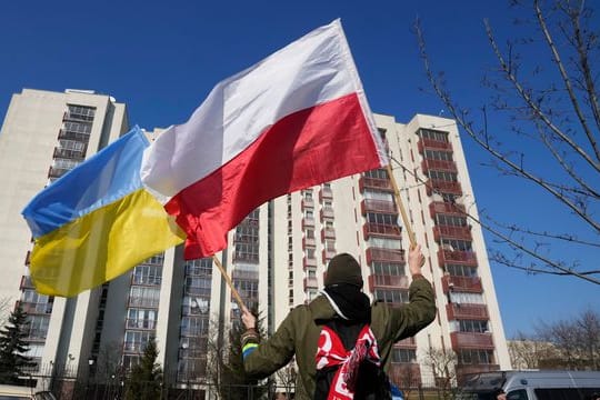 Ein Mann schwenkt während einer Demonstration in Warschau die ukrainische und die polnische Flagge vor einem Gebäude, in dem russische Diplomaten untergebracht sind.