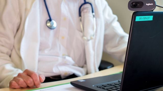 Ein Hausarzt sitzt während einer Videosprechstunde in seiner Praxis vor einem Laptop. Ein Hausarzt sitzt während einer Videosprechstunde in seiner Praxis vor einem Laptop.