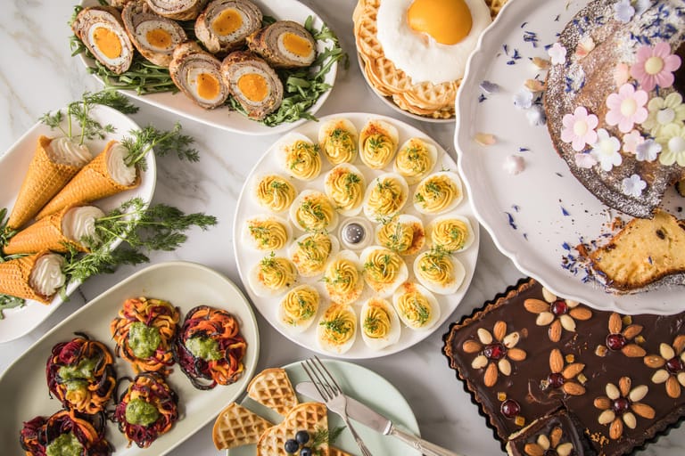 Lädt zum Verweilen ein: Ein Osterbrunch mit (im Uhrzeigersinn) Spiegelei-Waffeln, Babka, Mazurek, gefüllten Eiern, Gemüsenestern, Waffeln mit Frischkäse und Dill als "Karotten" und Schwalbennestern.