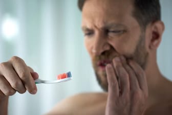 Ein Mann hält eine blutige Zahnbürste in der Hand.