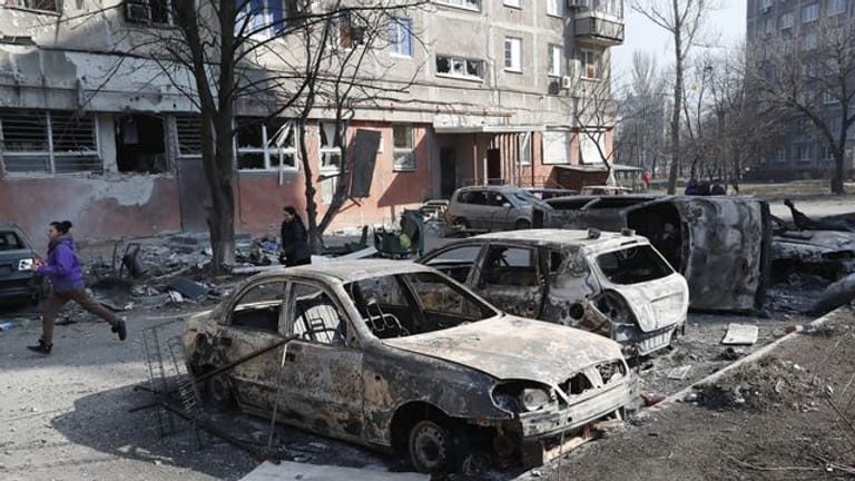 Menschen gehen an zerstörten Autos und Trümmern in Mariupol vorbei.