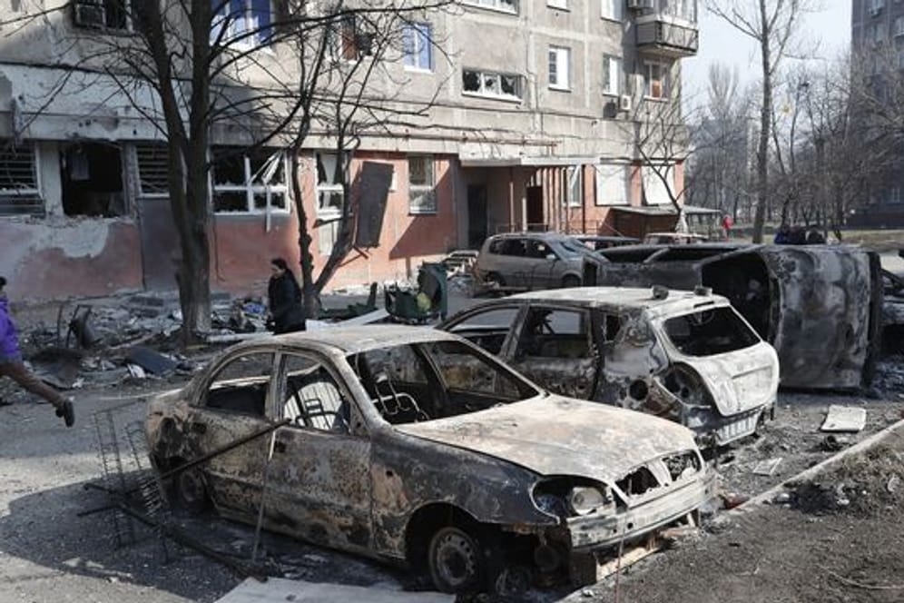 Menschen gehen an zerstörten Autos und Trümmern in Mariupol vorbei.