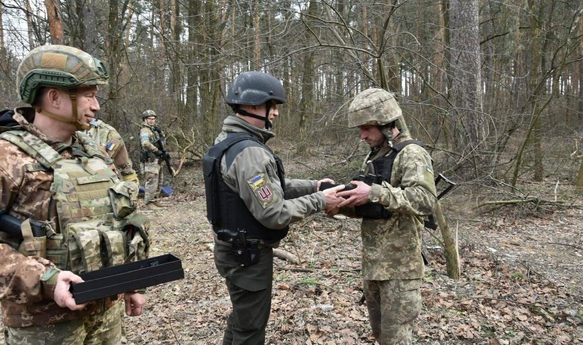 Der ukrainische Außenminister Oleksij Resnikow zeichnet einen Soldaten im Wald nahe von Kiew aus: Auch viele Zivilisten greifen zu den Waffen und verteidigen ihr Land.