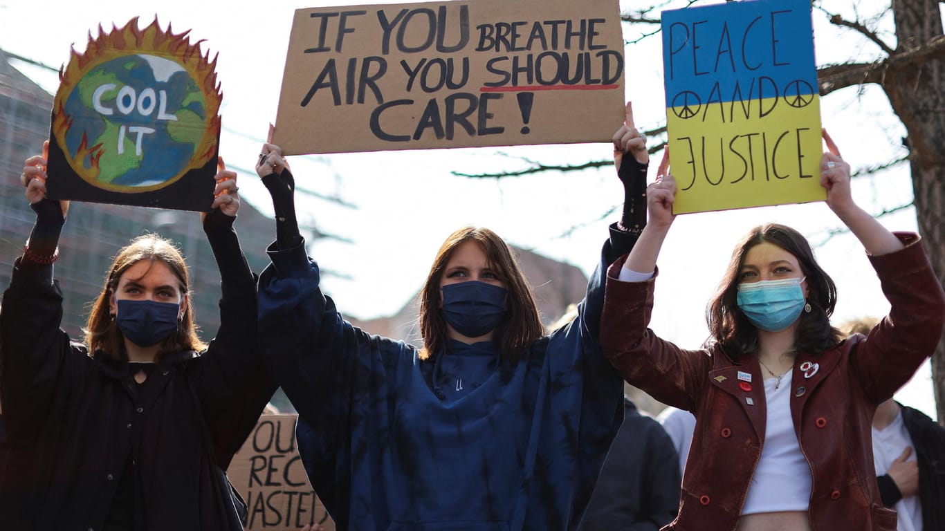 Demonstrierende halten Schilder mit den Aufschriften "Cool it", "If you breathe air you should care" und "Peace and justice" in den Händen: Mit dem Protest sollte auch ein Zeichen für Frieden gesetzt werden.