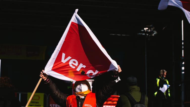 Eine streikende Arbeitnehmerin mit Verdi-Fahne (Symbolbild): In mehreren Städten sind Warnstreiks geplant.