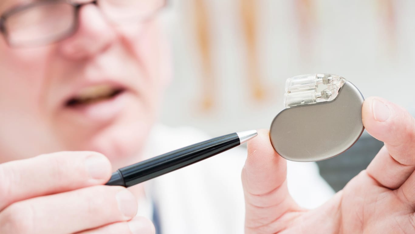 Mediziner hält einen Herzschrittmacher und zeigt mit einem Stift darauf