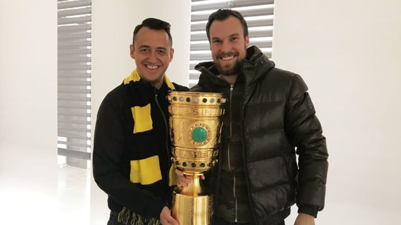 Gastronom Christopher Reinecke (l) und sein Geschäftspartner Kevin Großkreutz mit dem Duplikat des DFB-Pokals aus der gemeinsamen Kneipe.
