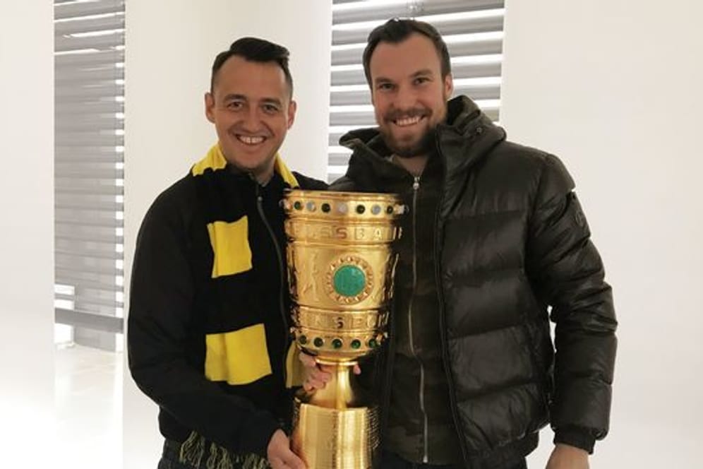 Gastronom Christopher Reinecke (l) und sein Geschäftspartner Kevin Großkreutz mit dem Duplikat des DFB-Pokals aus der gemeinsamen Kneipe.