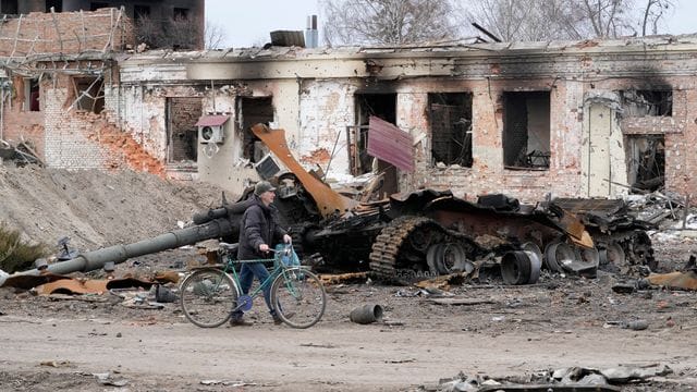 Ein Anwohner geht mit seinem Fahrrad in Trostjanez rund 400 km östlich von Kiew vor beschädigten Gebäuden und einem zerstörten Panzer entlang.