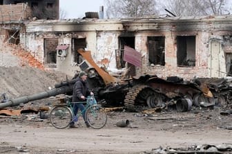Ein Anwohner geht mit seinem Fahrrad in Trostjanez rund 400 km östlich von Kiew vor beschädigten Gebäuden und einem zerstörten Panzer entlang.