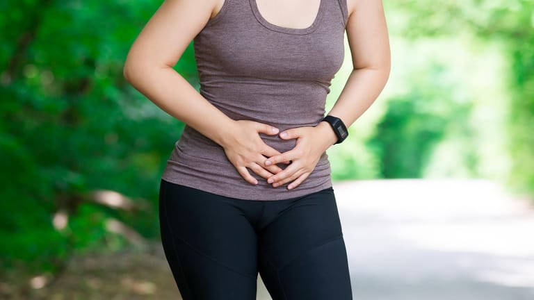 Frau hält sich wegen Schmerzen bei Joggen den Bauch: Wer mit einer Blasenschwäche joggen möchte, sollte darauf achten, dass regelmäßig der Beckenboden trainiert wird. So bleibt der Körper besser im Gleichgewicht.