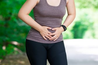 Frau hält sich wegen Schmerzen bei Joggen den Bauch: Wer mit einer Blasenschwäche joggen möchte, sollte darauf achten, dass regelmäßig der Beckenboden trainiert wird. So bleibt der Körper besser im Gleichgewicht.