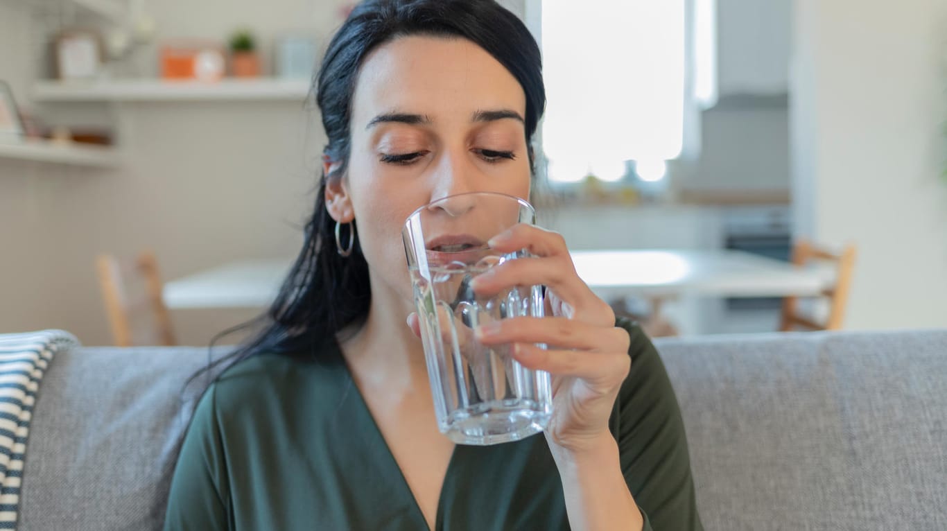 Eine Frau führt ein Wasserglas zum Mund.