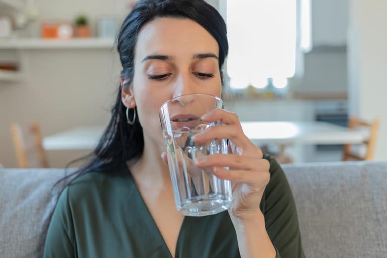 Eine Frau führt ein Wasserglas zum Mund.