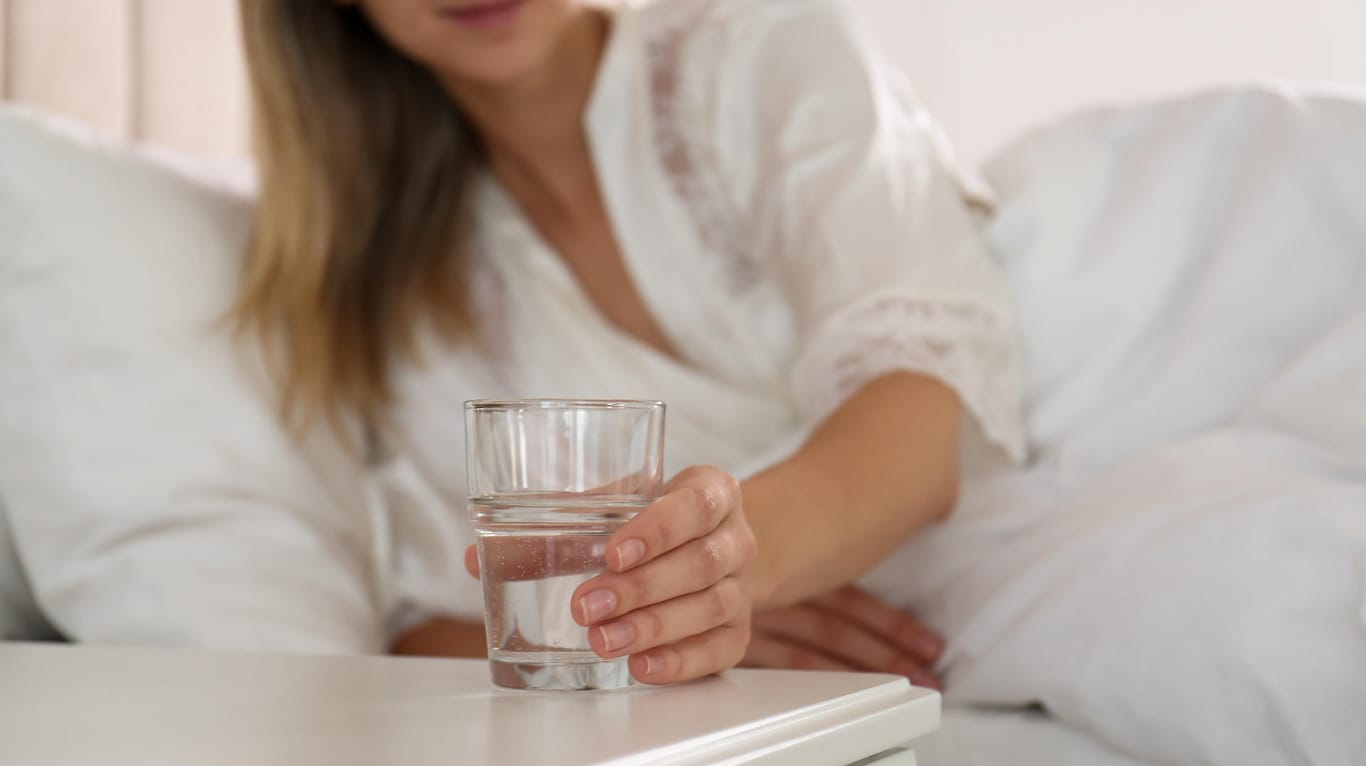 Frau greift nach Wasserglas auf Nachttisch.