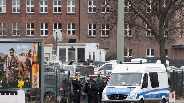 Polizeikräfte stehen vor dem Gelände eines Gebrauchtwagenhändlers.